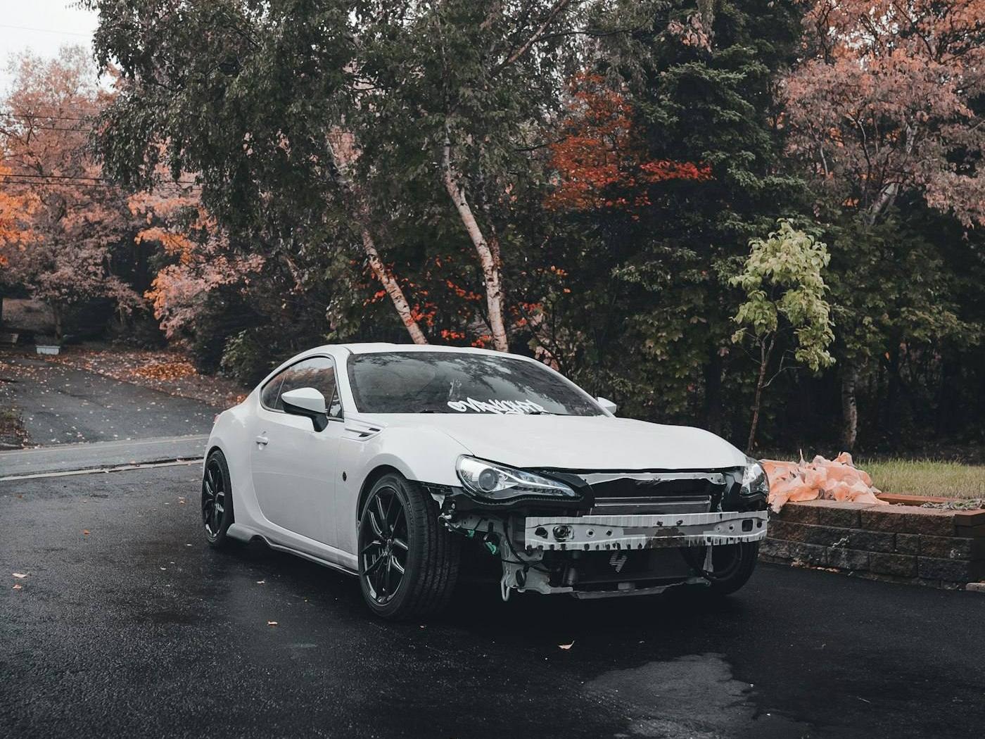 A white car with a damaged front bumper before repair