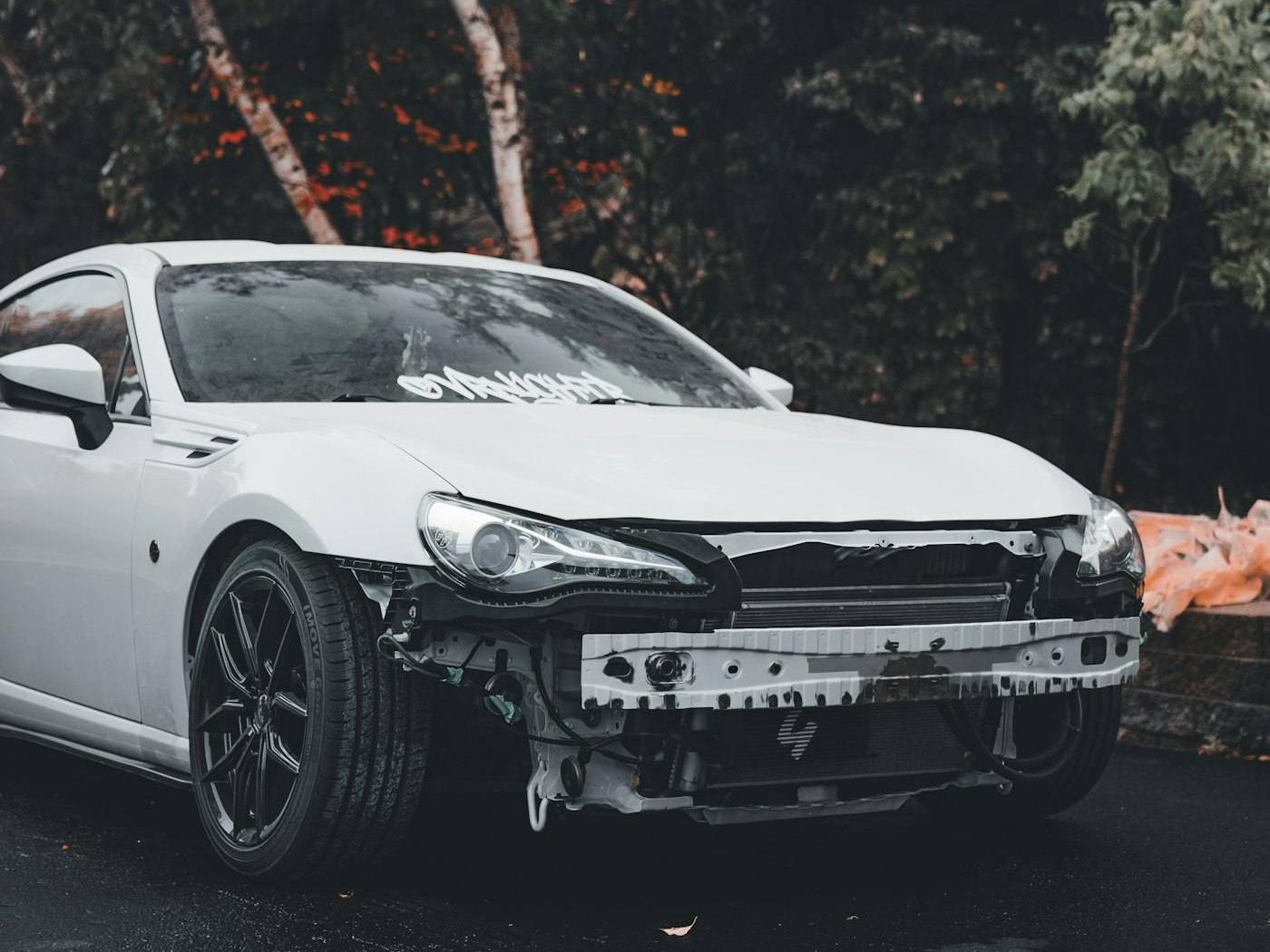 A white car with the front bumper removed during repair
