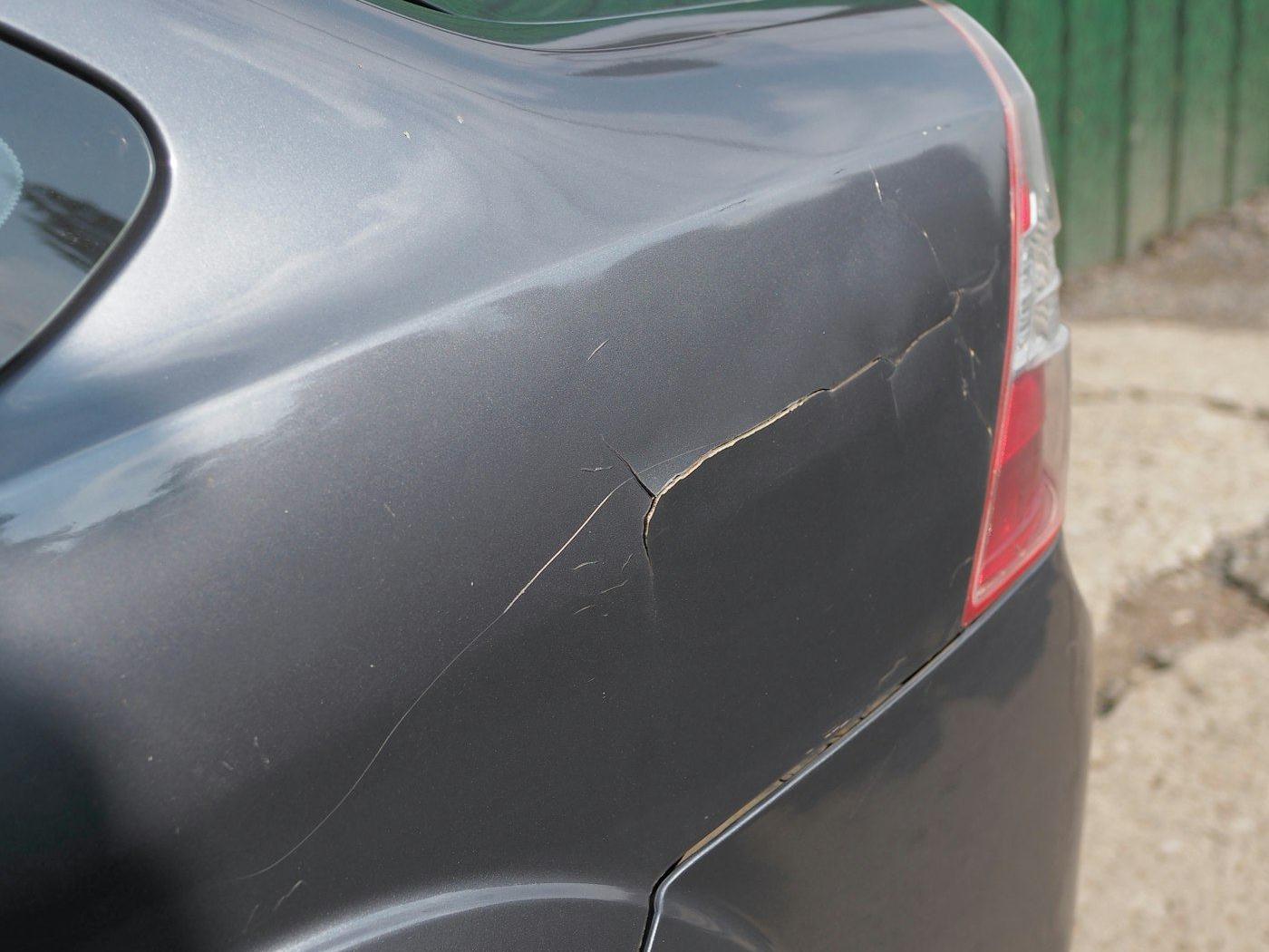 A grey car fender with a dent and cracked paint before repair