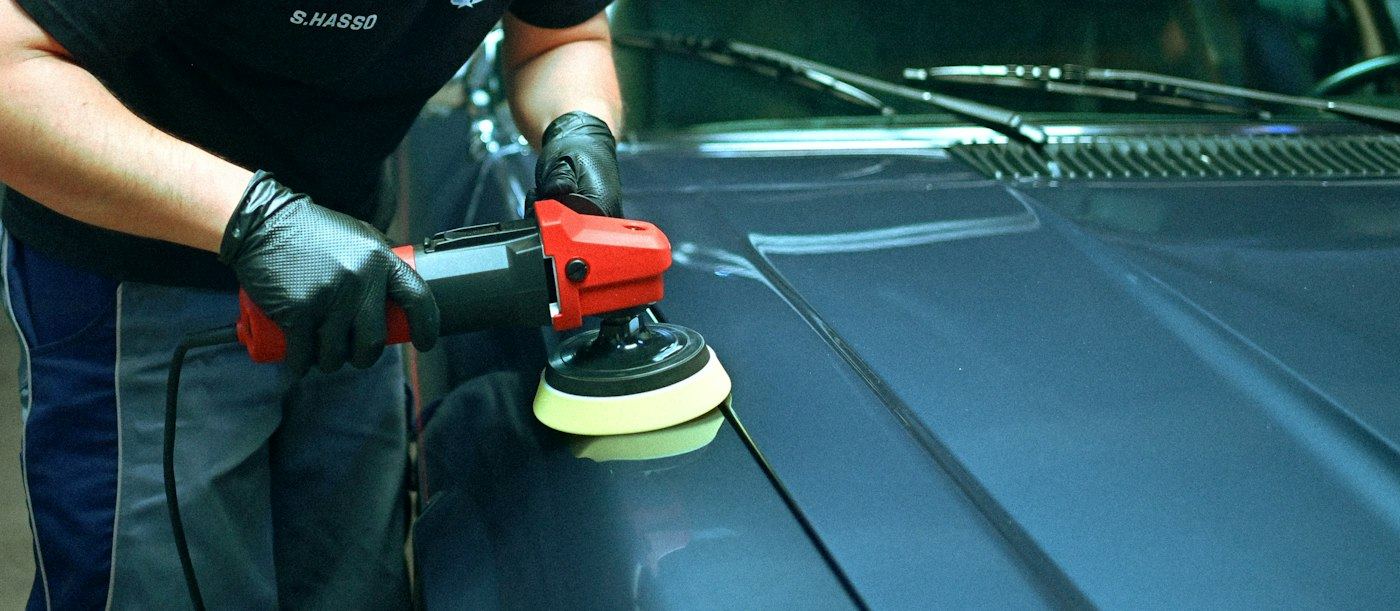 Polishing a blue car's hood with an orbital buffer
